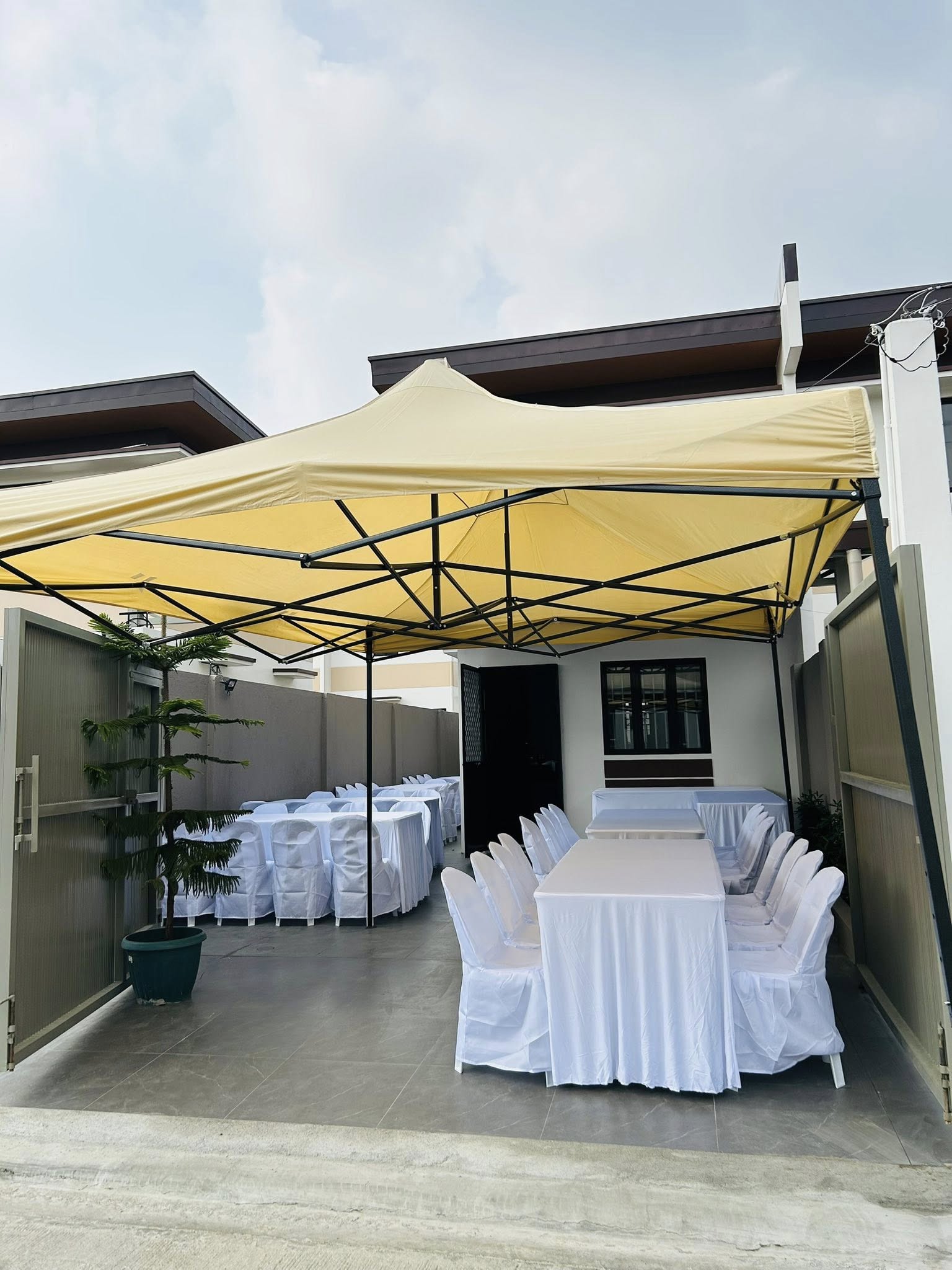 Easy Rental event setup — yellow-beige pop-up canopy with white chair slipcovers and draped tables on a tiled home courtyard